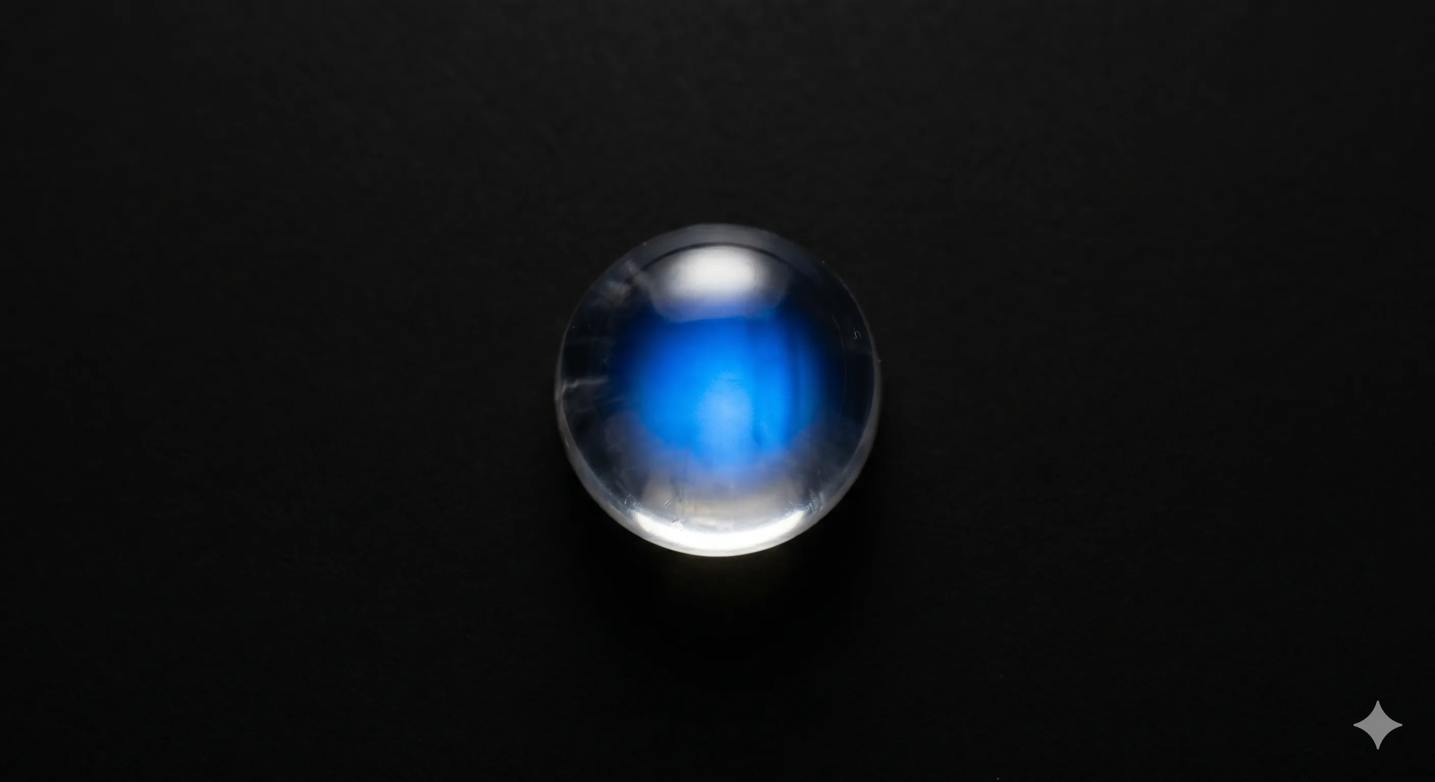A colorless Ceylon moonstone cabochon under direct lighting showing a bright centered blue adularescence